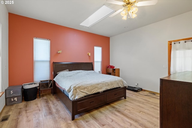 bedroom featuring ceiling fan, light hardwood / wood-style flooring, and a skylight