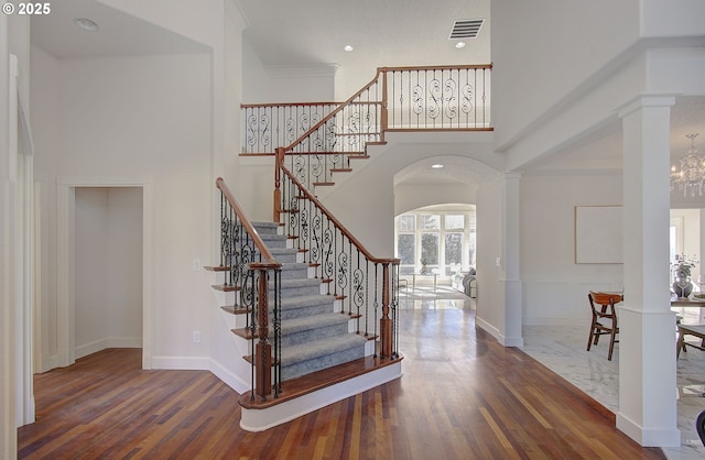staircase with a high ceiling, wood finished floors, and visible vents