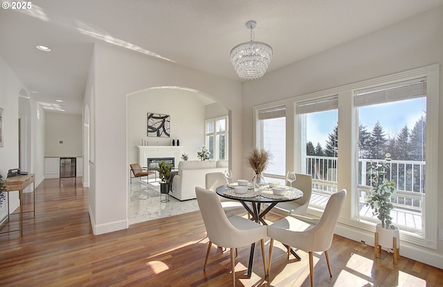dining room with a wealth of natural light, a glass covered fireplace, arched walkways, and a chandelier