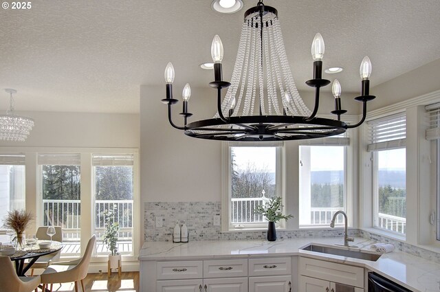kitchen featuring white cabinets, a wealth of natural light, a notable chandelier, and a sink