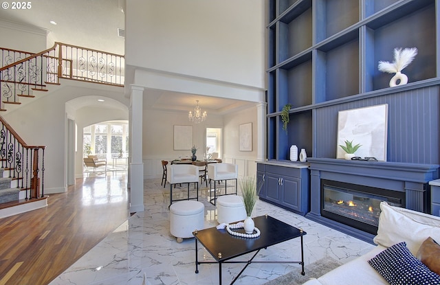 living area with arched walkways, a towering ceiling, a notable chandelier, marble finish floor, and stairs