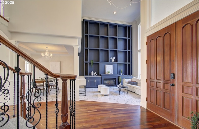 foyer entrance with a glass covered fireplace, an inviting chandelier, wood finished floors, stairs, and ornamental molding
