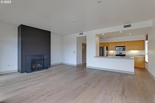 unfurnished living room with sink, light wood-type flooring, and a fireplace