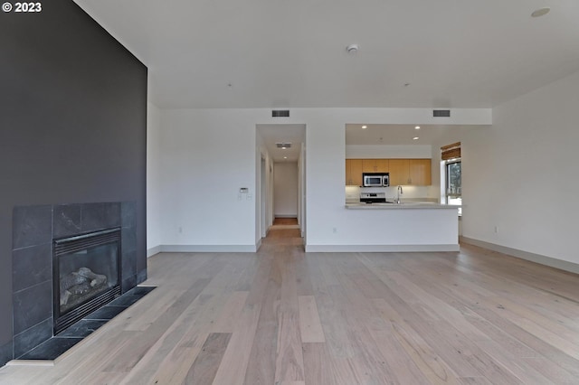 unfurnished living room featuring a tile fireplace, sink, and light wood-type flooring