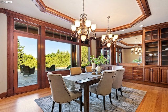 dining room with a tray ceiling, ornamental molding, light wood-type flooring, and an inviting chandelier