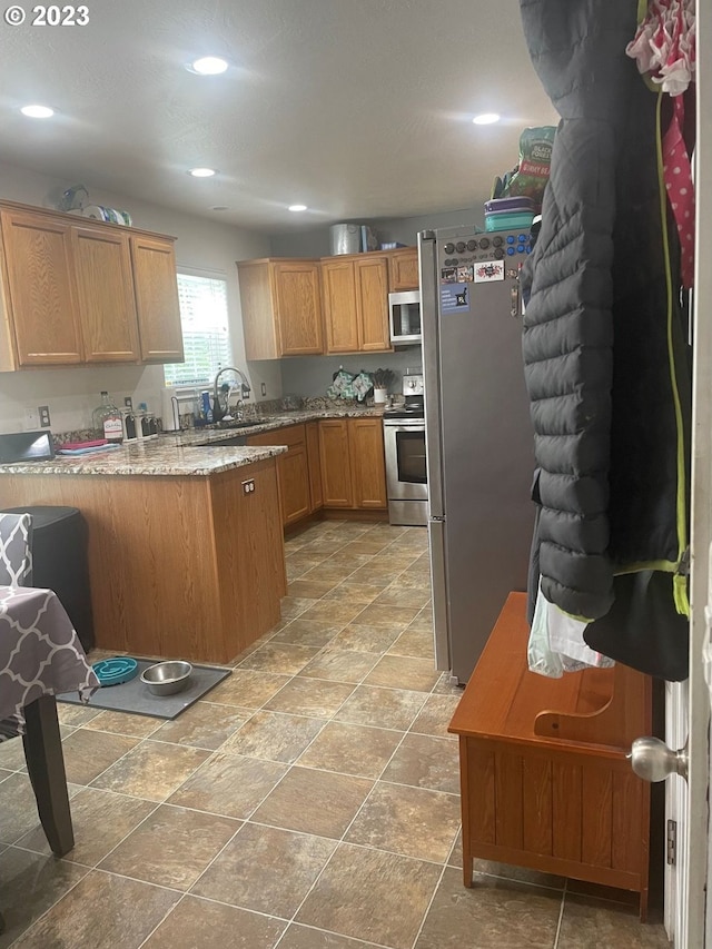 kitchen with light stone countertops, kitchen peninsula, appliances with stainless steel finishes, sink, and light tile floors