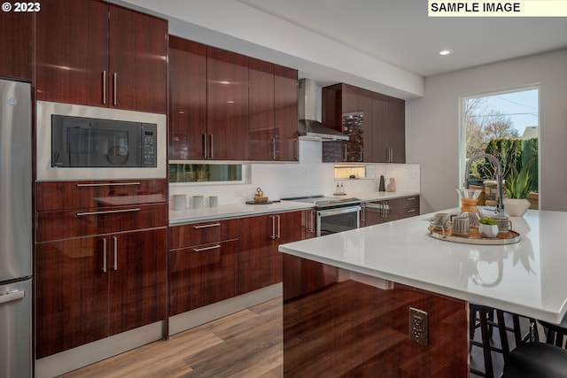 kitchen with a kitchen breakfast bar, stainless steel appliances, sink, wall chimney range hood, and backsplash