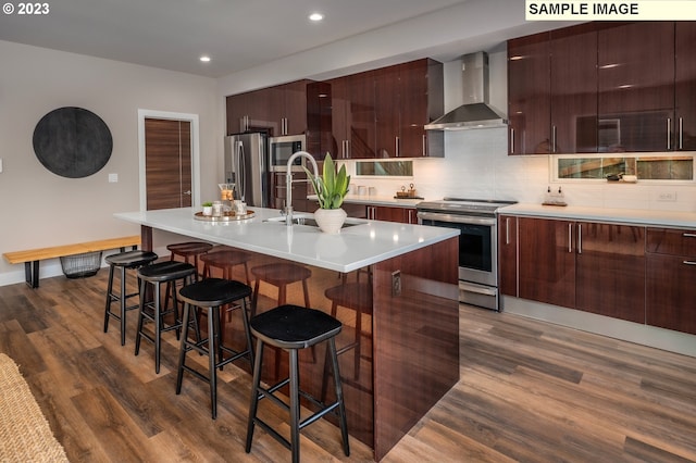 kitchen with stainless steel appliances, wall chimney range hood, a breakfast bar area, and a center island with sink