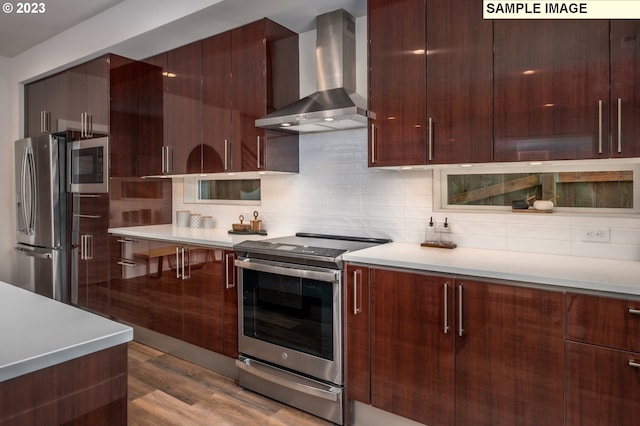 kitchen featuring stainless steel appliances, light wood-type flooring, wall chimney range hood, and tasteful backsplash