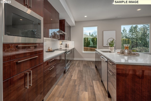 kitchen with stainless steel appliances, an island with sink, light hardwood / wood-style floors, decorative backsplash, and sink