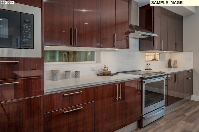 kitchen featuring stainless steel electric stove, wall chimney range hood, built in microwave, and wood-type flooring