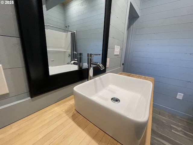 full bath with a sink, hardwood / wood-style floors, and wood walls