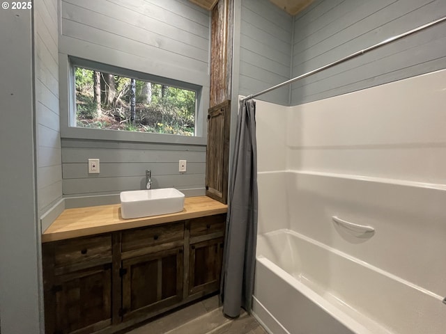 bathroom with vanity, wooden walls, and shower / bath combo with shower curtain