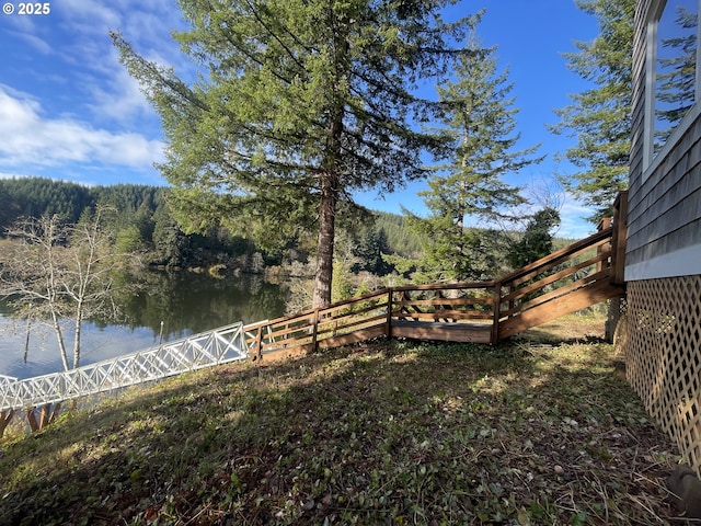 view of yard featuring a wooded view, a water view, and fence