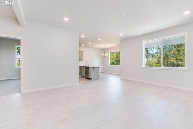 unfurnished living room with beam ceiling, a chandelier, sink, and light hardwood / wood-style flooring