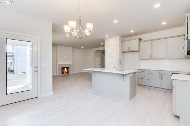 kitchen with sink, tasteful backsplash, hanging light fixtures, a center island with sink, and light hardwood / wood-style flooring