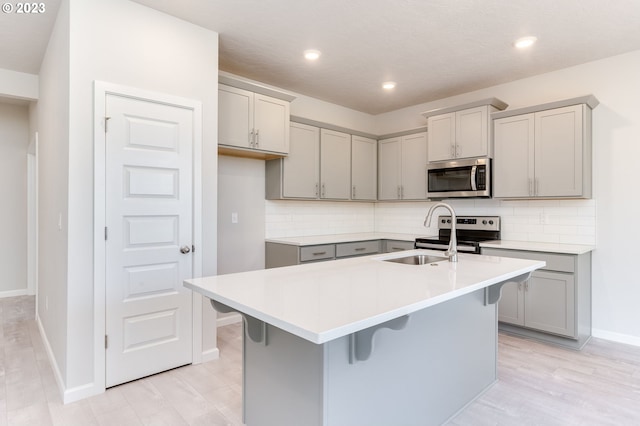 kitchen featuring sink, appliances with stainless steel finishes, gray cabinetry, a kitchen breakfast bar, and a center island with sink