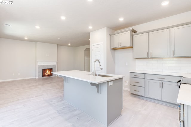 kitchen featuring sink, tasteful backsplash, a center island with sink, gray cabinets, and a fireplace