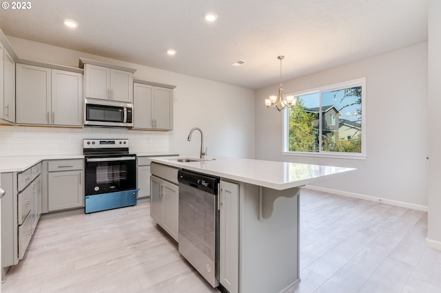 kitchen with gray cabinets, appliances with stainless steel finishes, sink, decorative backsplash, and a center island with sink