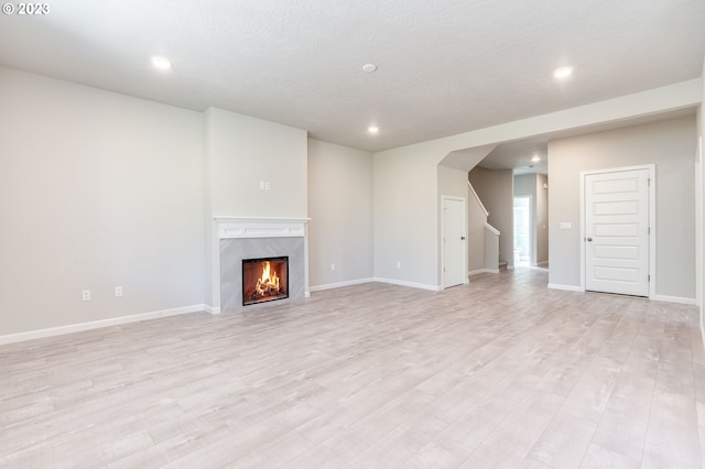 unfurnished living room with a premium fireplace, a textured ceiling, and light hardwood / wood-style flooring