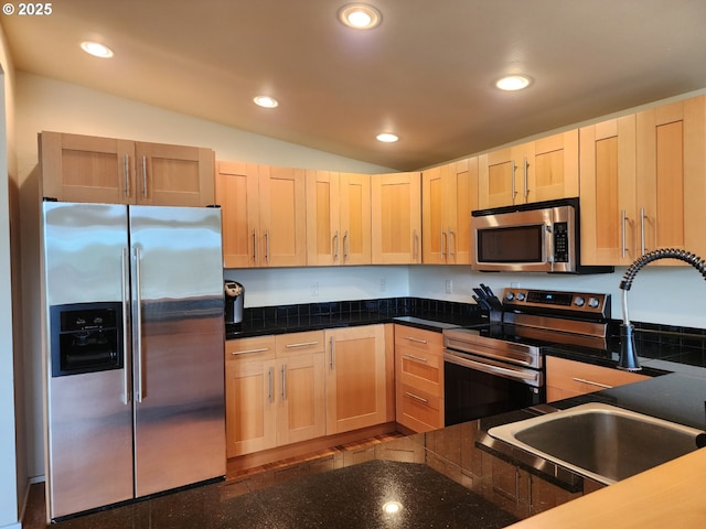 kitchen featuring dark countertops, light brown cabinets, appliances with stainless steel finishes, and a sink