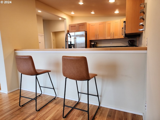 kitchen with a peninsula, a breakfast bar, recessed lighting, stainless steel fridge with ice dispenser, and light wood-style floors