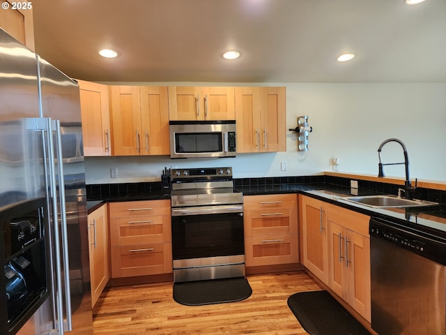 kitchen with recessed lighting, dark countertops, a sink, light wood-style floors, and stainless steel appliances