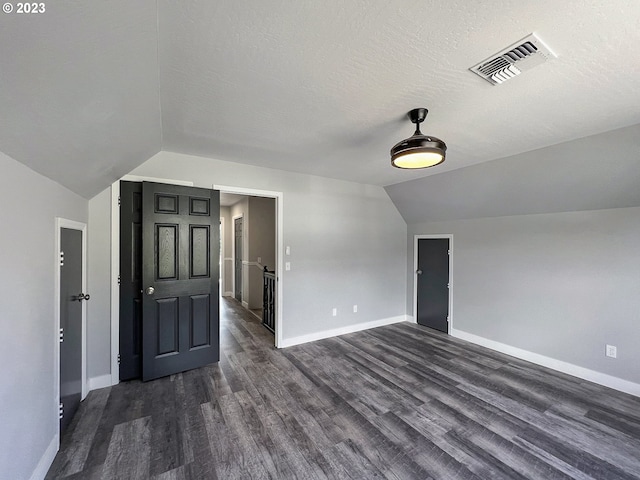 bonus room with a textured ceiling, dark wood-type flooring, and vaulted ceiling