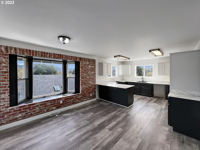 kitchen with brick wall, wood-type flooring, white cabinetry, and sink