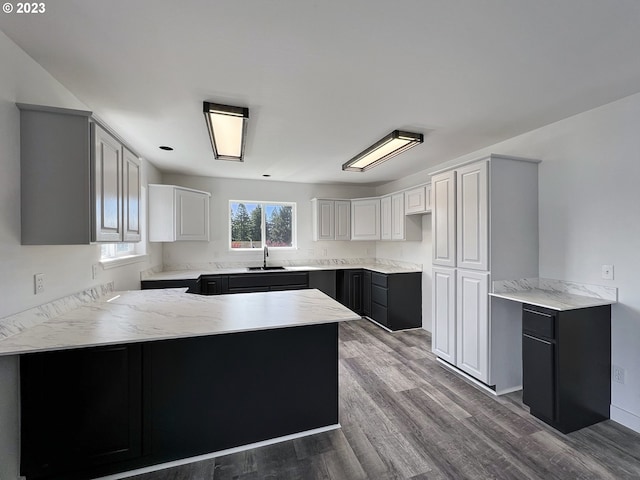 kitchen with hardwood / wood-style floors, white cabinets, kitchen peninsula, and sink