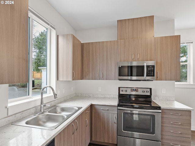 kitchen featuring a healthy amount of sunlight, light stone countertops, stainless steel appliances, and sink