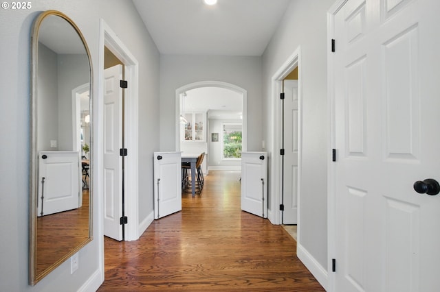 corridor featuring arched walkways, wood finished floors, and baseboards