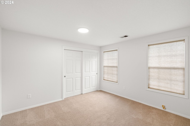 unfurnished bedroom featuring multiple windows, a closet, and light colored carpet