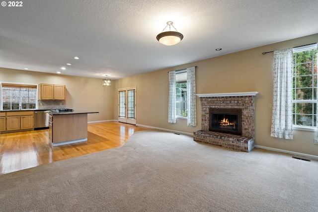 kitchen with a textured ceiling, a brick fireplace, light hardwood / wood-style floors, stainless steel dishwasher, and light brown cabinets