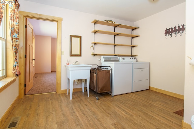 clothes washing area with washing machine and dryer and light hardwood / wood-style flooring