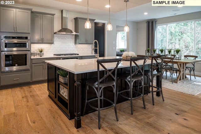 kitchen featuring pendant lighting, stainless steel appliances, light hardwood / wood-style flooring, and wall chimney range hood