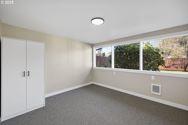 unfurnished bedroom featuring a closet, dark carpet, visible vents, and baseboards