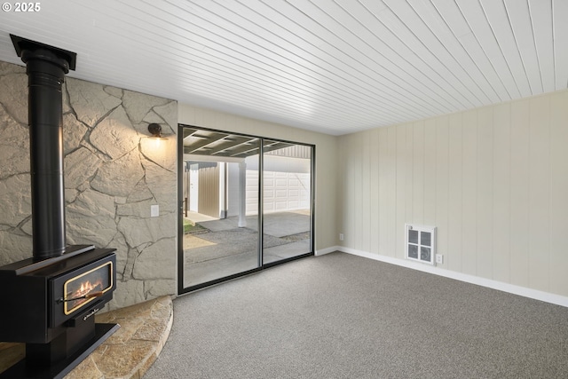 unfurnished living room featuring carpet floors, a wood stove, visible vents, and baseboards