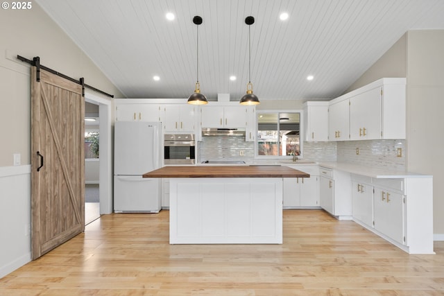 kitchen with lofted ceiling, a barn door, freestanding refrigerator, wood counters, and oven