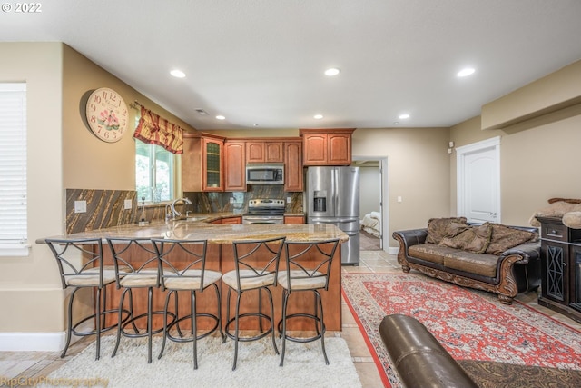 kitchen featuring appliances with stainless steel finishes, light tile flooring, tasteful backsplash, a breakfast bar, and sink