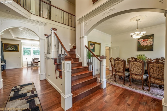 stairway with dark hardwood / wood-style flooring, crown molding, a notable chandelier, a textured ceiling, and decorative columns