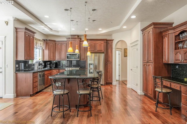 kitchen featuring a tray ceiling, appliances with stainless steel finishes, wood-type flooring, a kitchen island, and a breakfast bar area