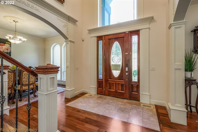 entryway with dark tile floors, ornamental molding, decorative columns, and an inviting chandelier