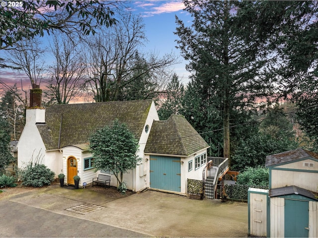 view of front facade featuring an outbuilding, stucco siding, a chimney, and a shed