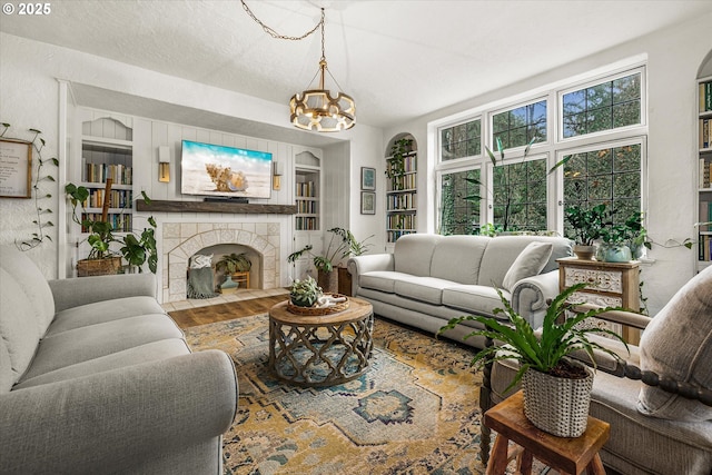 living area with built in features, an inviting chandelier, a textured ceiling, wood finished floors, and a tile fireplace