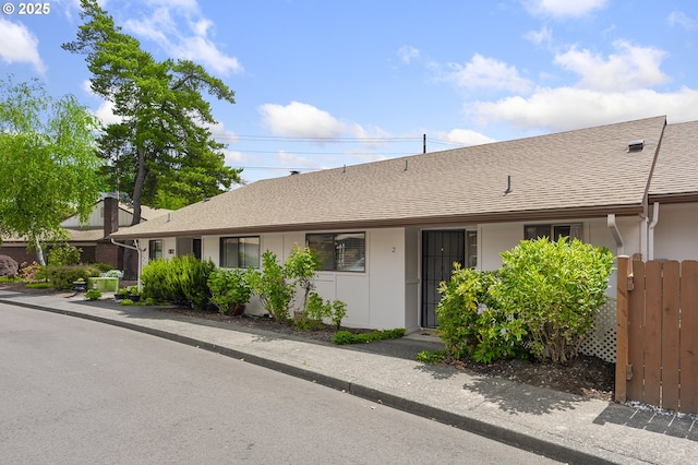 ranch-style house with roof with shingles, stucco siding, and fence