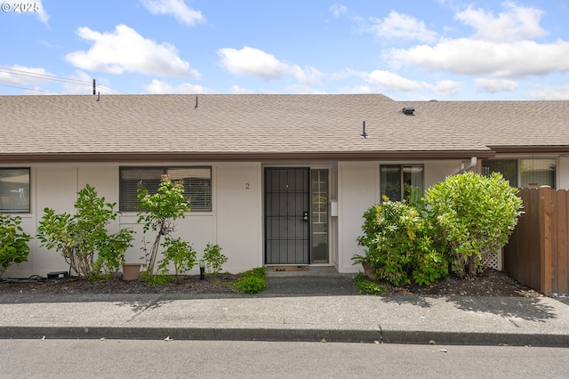 view of exterior entry with a shingled roof, fence, and stucco siding