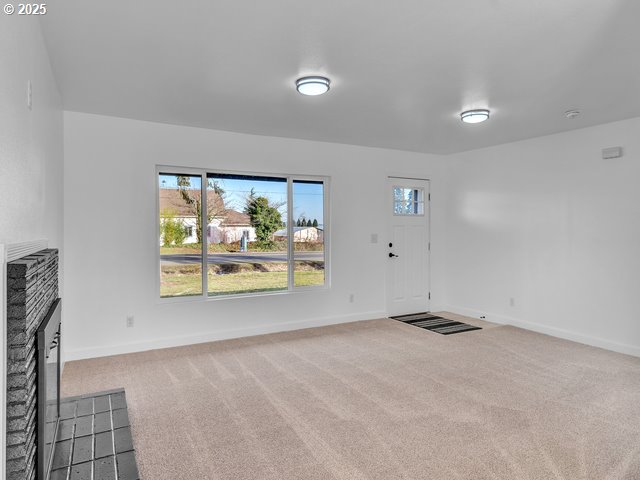 unfurnished living room featuring carpet floors and a brick fireplace