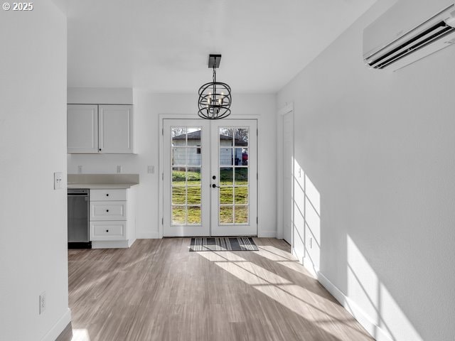 unfurnished dining area with an inviting chandelier, a wall mounted air conditioner, light hardwood / wood-style flooring, and french doors