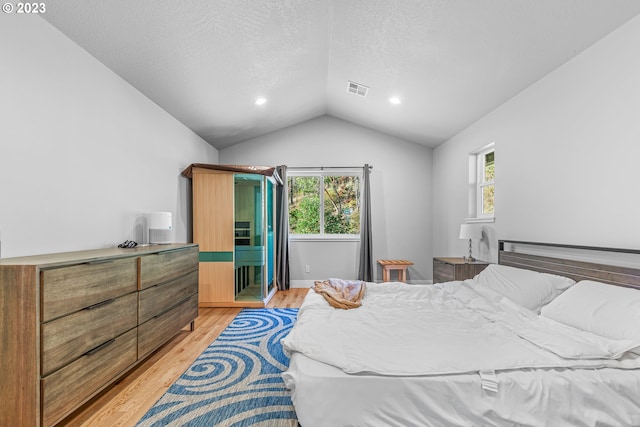 bedroom with vaulted ceiling, light hardwood / wood-style floors, and a textured ceiling